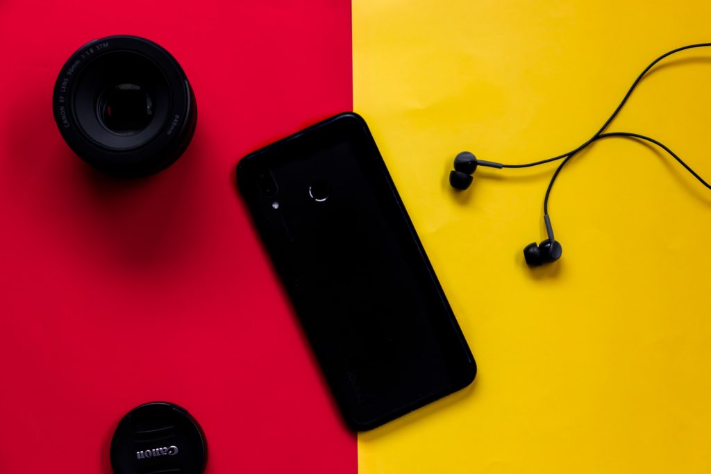 A phone, earphones, and speakers laid out on a red and yellow table. 