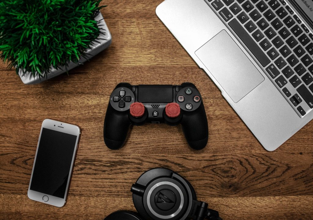 A controller, phone, and laptop on a desk.
